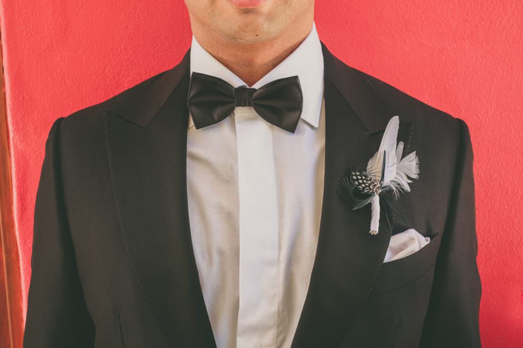 a groom with a feather button hole against a red wall at villa vivante coffs harbour