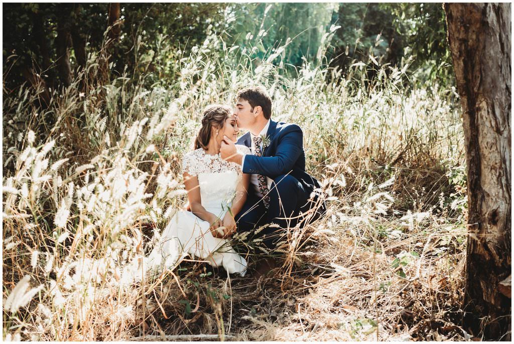 a groom tenderly kisses his wife forehead as she closes her eyes in the long Darwin grass