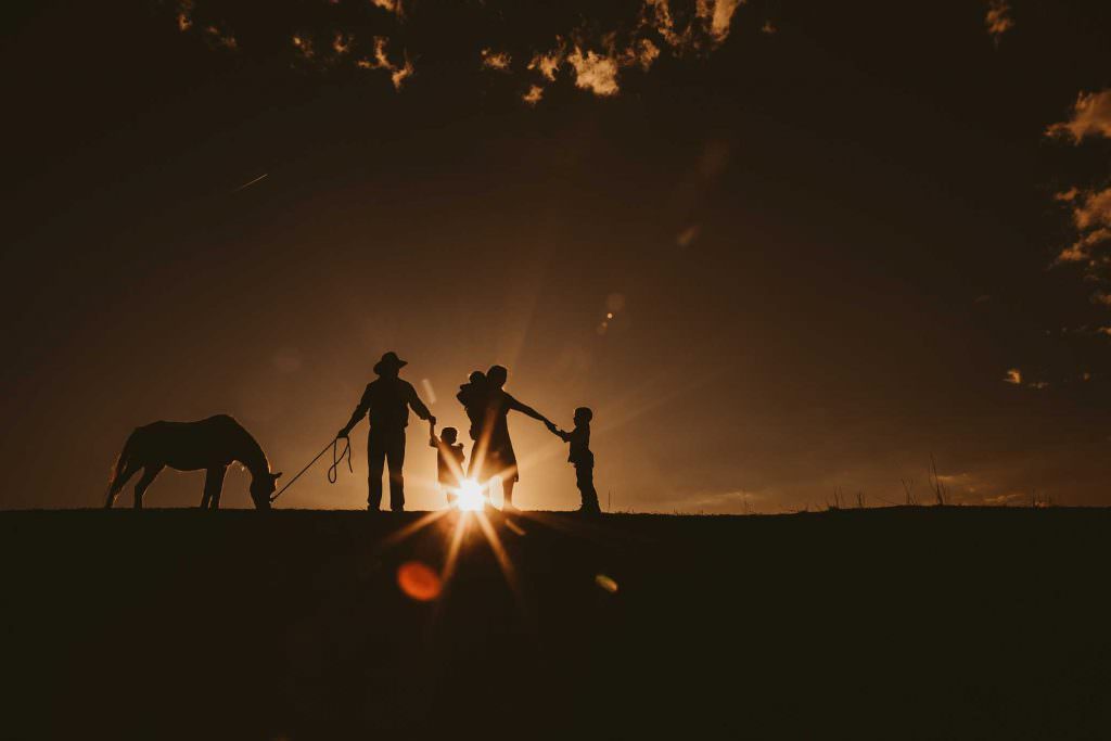 a sun sets over the hills as a family walks with their horse