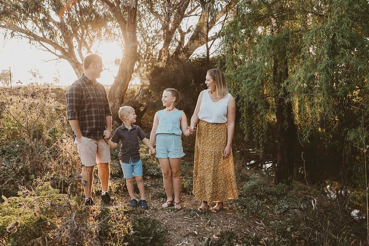 family of four laughs at each as the sun sets at a creek in the peel valley