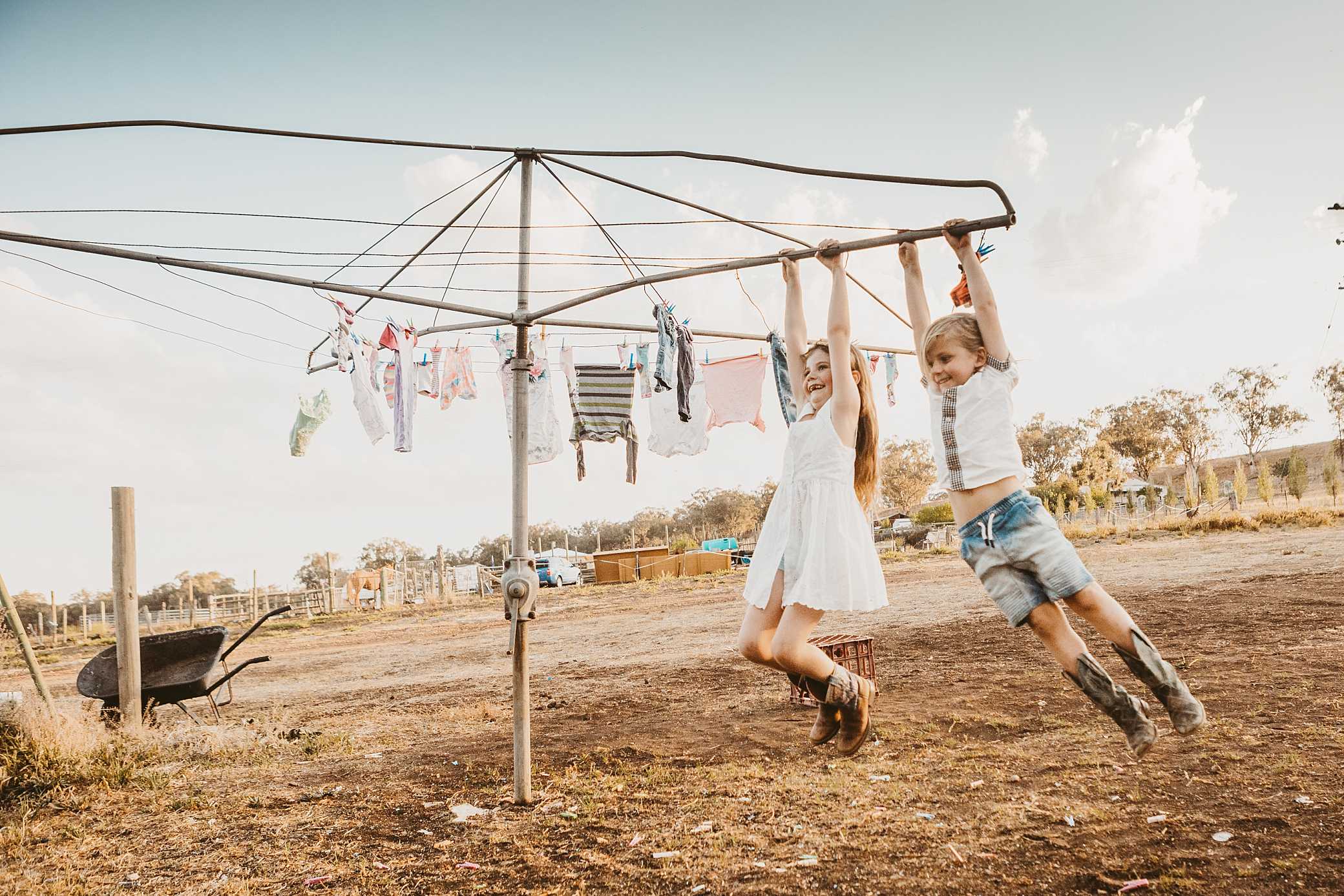 two kids swinging on a Hillshoist in country NSW. There is baby clothes on the clothes line just outside of Tamworth NSW