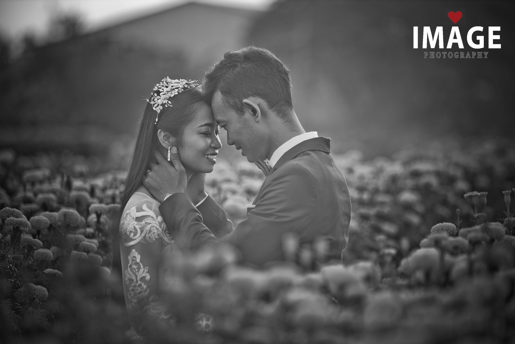 a black and white image of a bride with flowers around her is held by her new husband