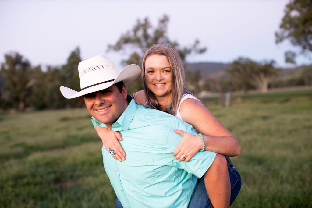 piggy back ride for a prewedding shoot the guy is wearing a cowboy hat ythey are on a farm