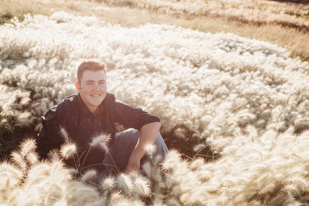 white fluffy grass in bendemeer shine as the sun hits it as a teenage boy sits with his knee up