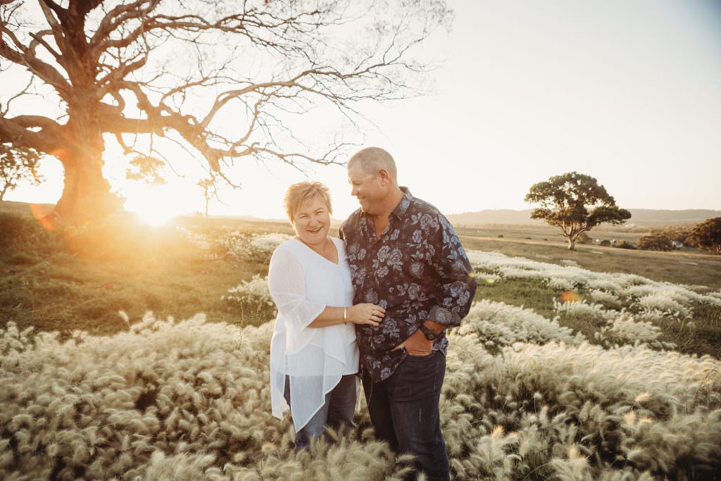 sun setting through a dead tree as a husband smiles at his wife with the hills of Bendemeer for a tamworth family portrait