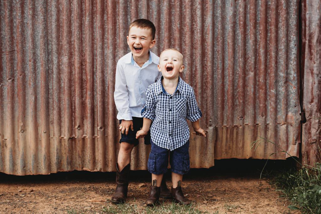 laughs all around for two young boys against a rusty farm shed near Tamworth. the young kids are wearing cowboy boots for their family portrait