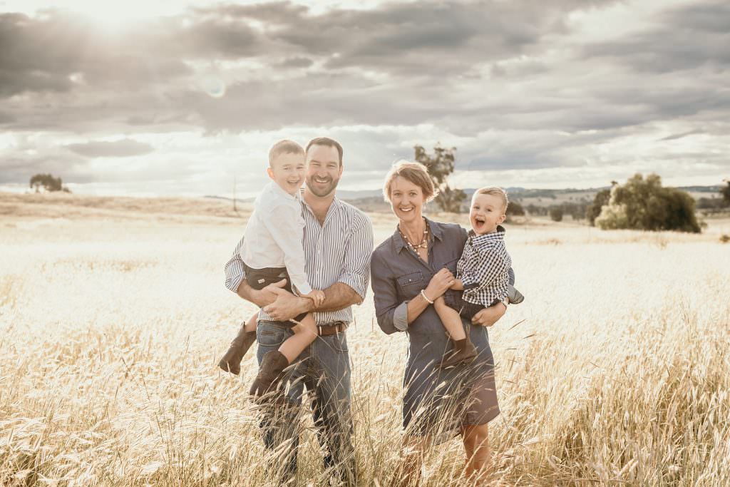 golden long grass as the sun sets behind a Tamworth family for their portrait. The boys are laughing as their parents hold them