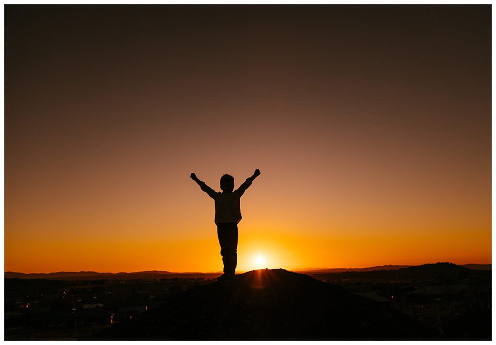 a young boy cheers as the sun sets in the background. the background is orange