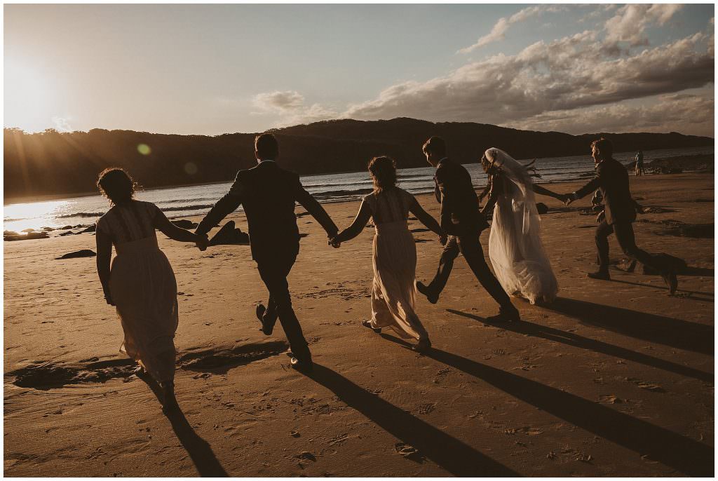 bridal party running on the beach as their shadows follow them near Forster