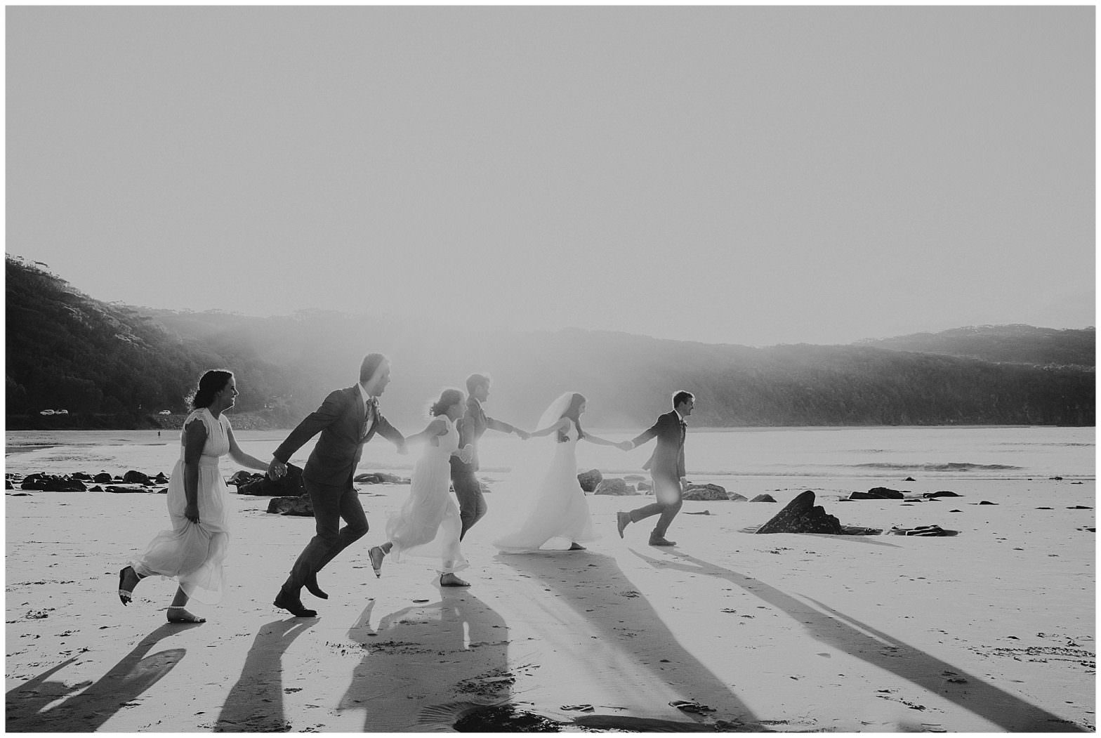 black and white bridal party running at the beach as the suns rays set in the background