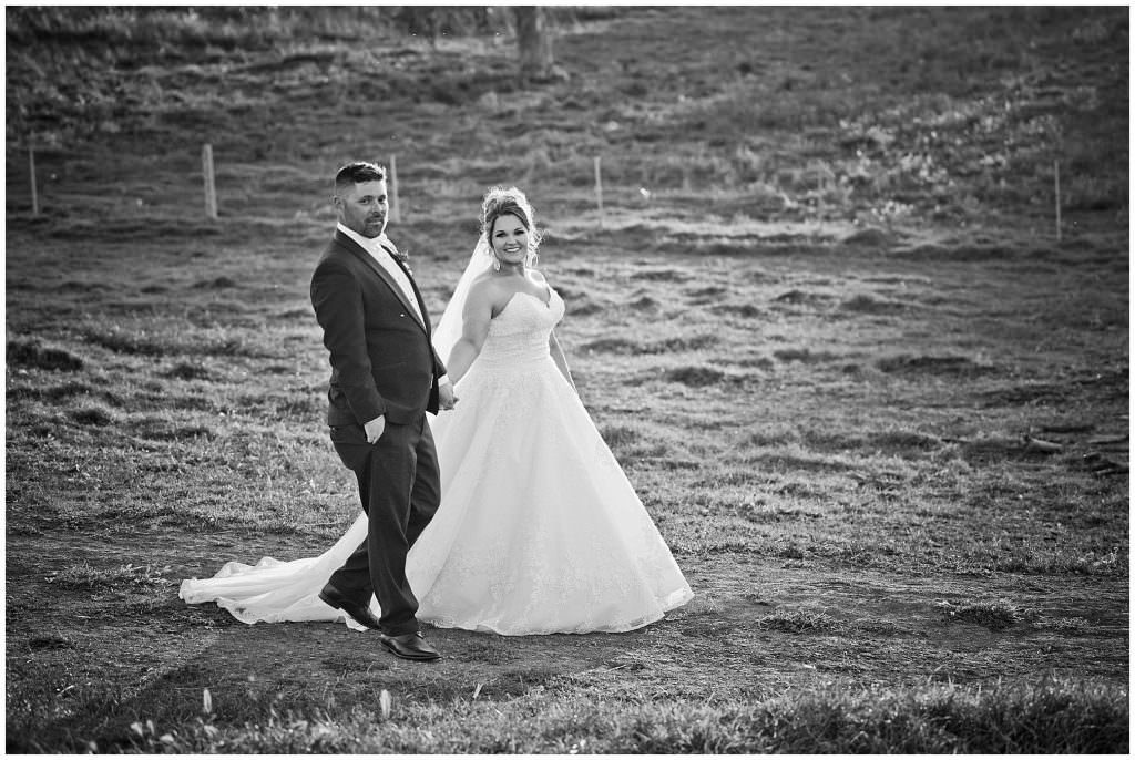 black and white photograph of a bridal couple walking as the sun sets in the background