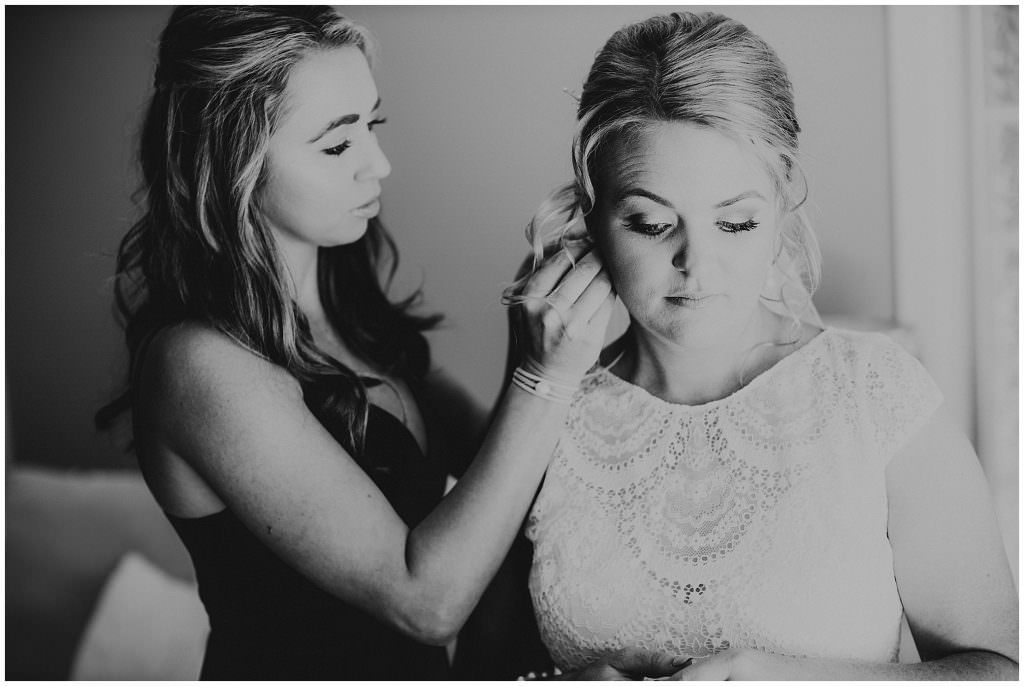 black and white photo of a bridesmaid helping her bride put her earrings on