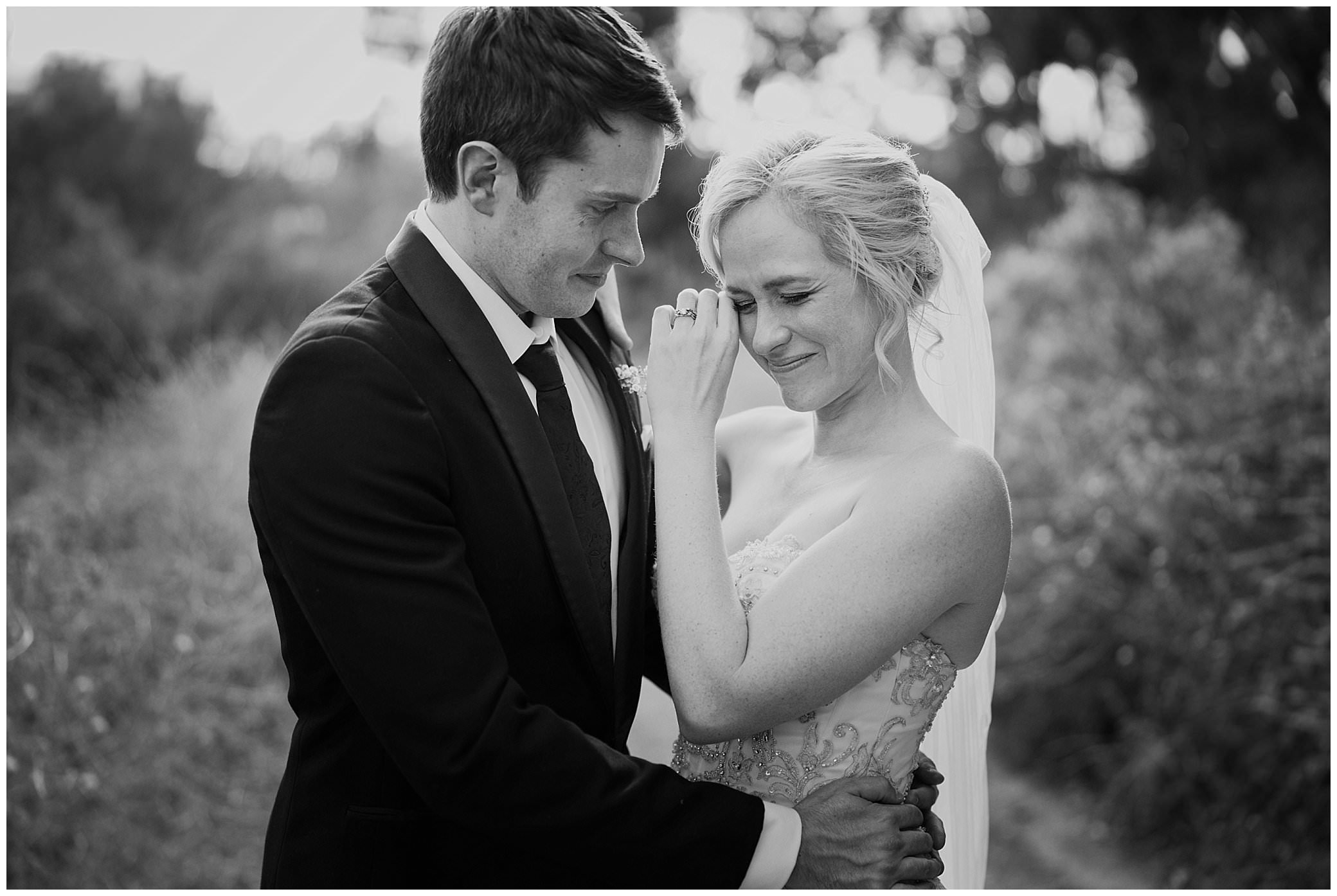 black and white photo of a bride and groom hug as a bride cries down a country road for real emotion on a wedding day as captured by Karissa Tamworth NSW wedding photographer