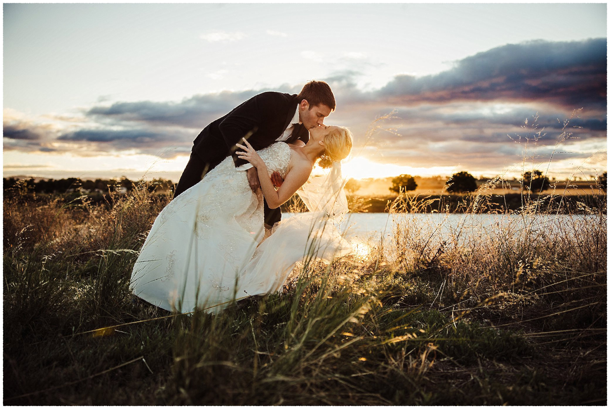 as the sun sets over Tangarratta dam a newly married couple kiss as the sun goes down amongst long golden grass