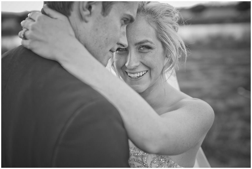 black and white of a bride with her hands around her husbands neck as she smiles at her Tamworth wedding photographer