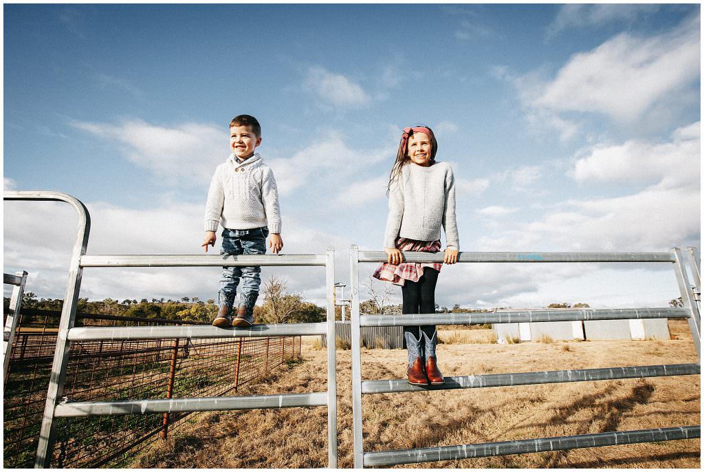 siblings climbing cattle yards as the Tamworth blue sky is in the backgorund as the kids smile at Tamworth's best family photographer