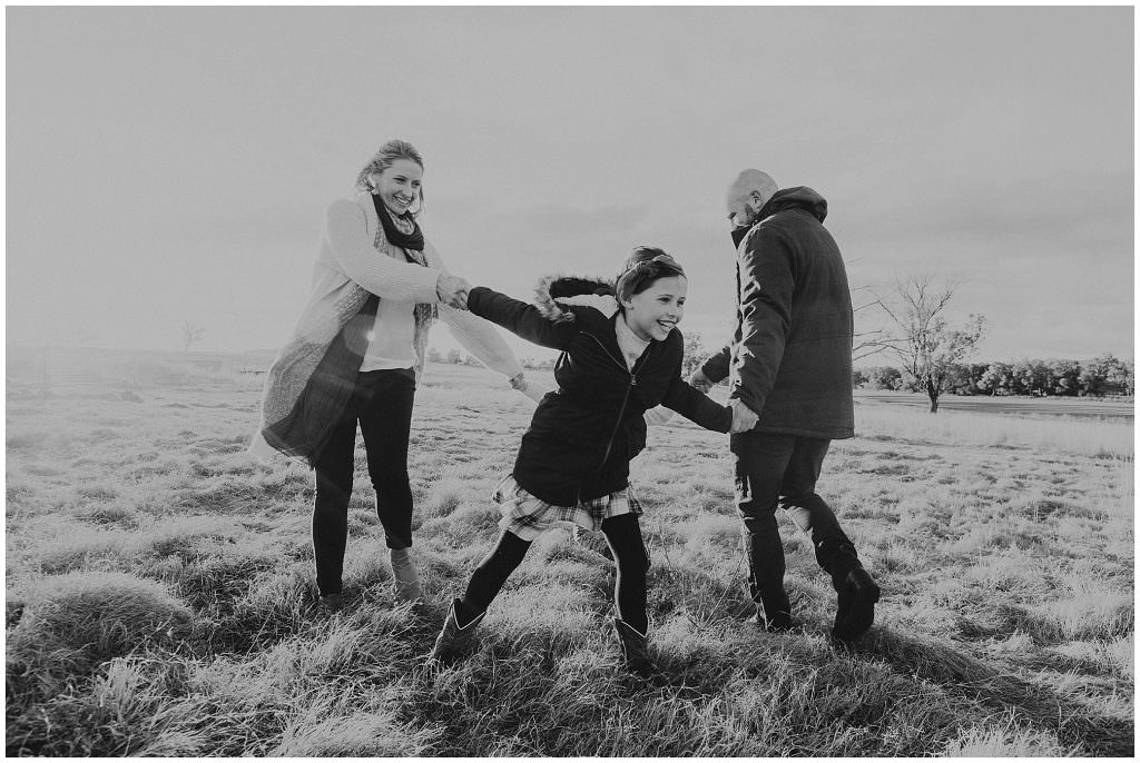 tamworth best family photographer shoots a black and white photo of a family of four running in circles as the sun sets over their shoulders they are laughing