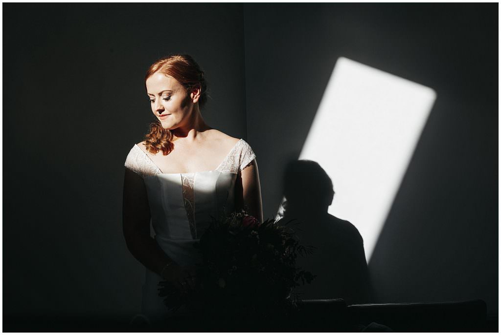 the light from a sky light highlights a bride with red hair on her wedding day