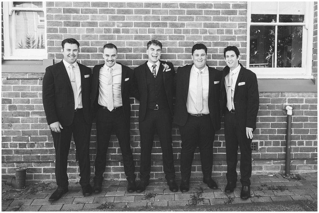 all smiles for the groomsmen black and white photo against an older brick wall at a house