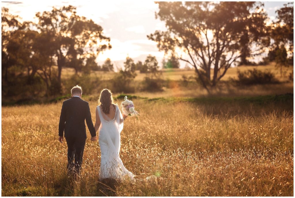 sunsets golden grass as a bride and groom walk away. The sun kisses her brides bouquet from posies florist Tamworth