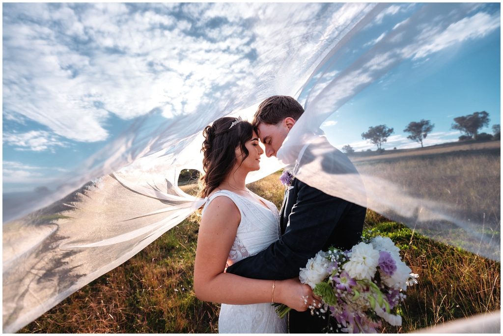 under a bridal veil and blue skies a couple hug into each other at Tamworth