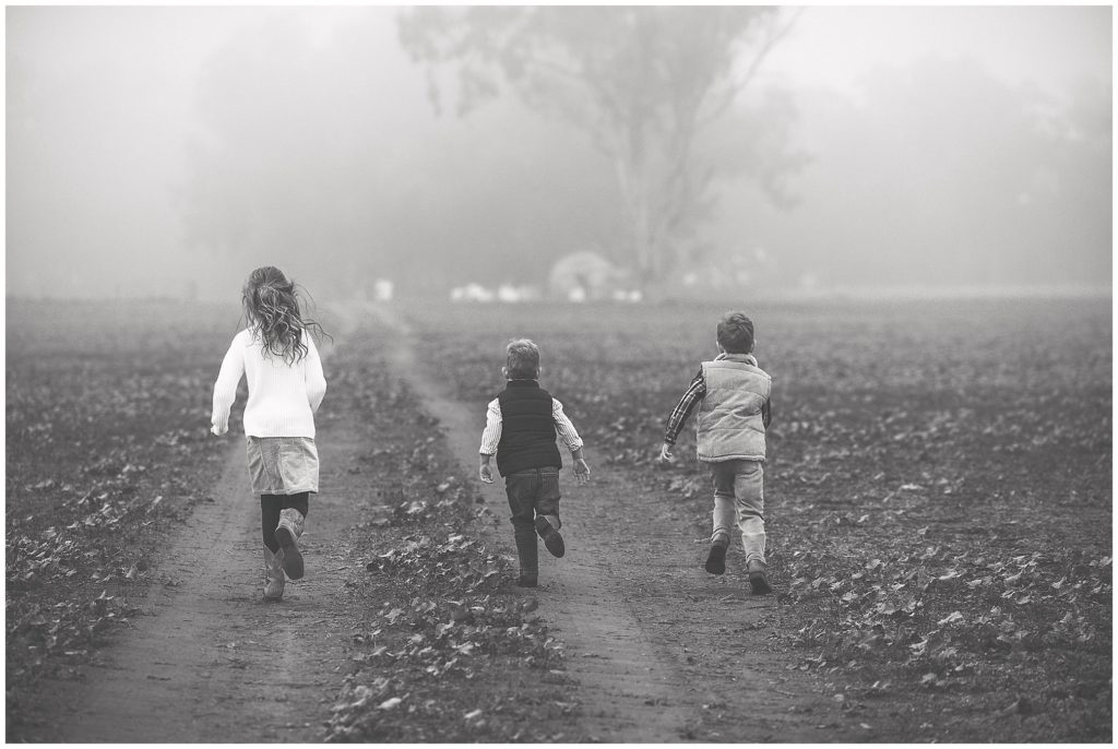 a foggy morning as 3 children run down a cowra country road for the family portrait