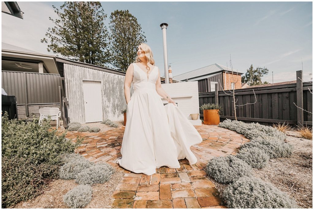 vintage tones in the back garden of Querencia airbnb as a bride hold her dress and looks into a Tamworth blue sky