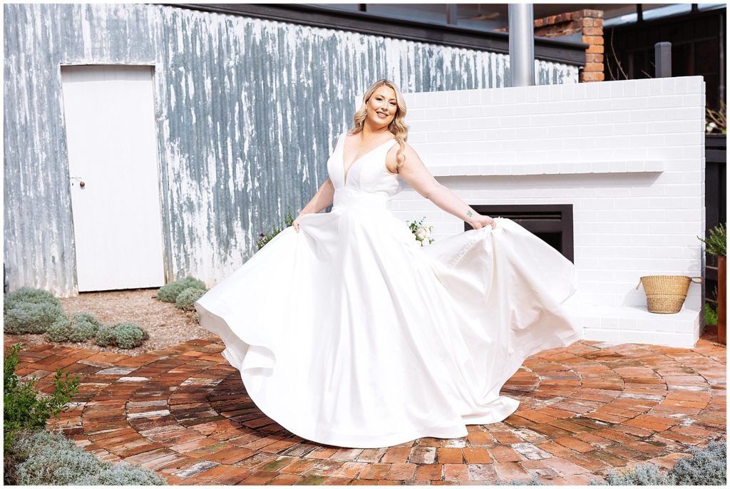 a bride in a white dress dancers in the back garden of Querencia airbnb a white fireplace and corrugated shed is in the background