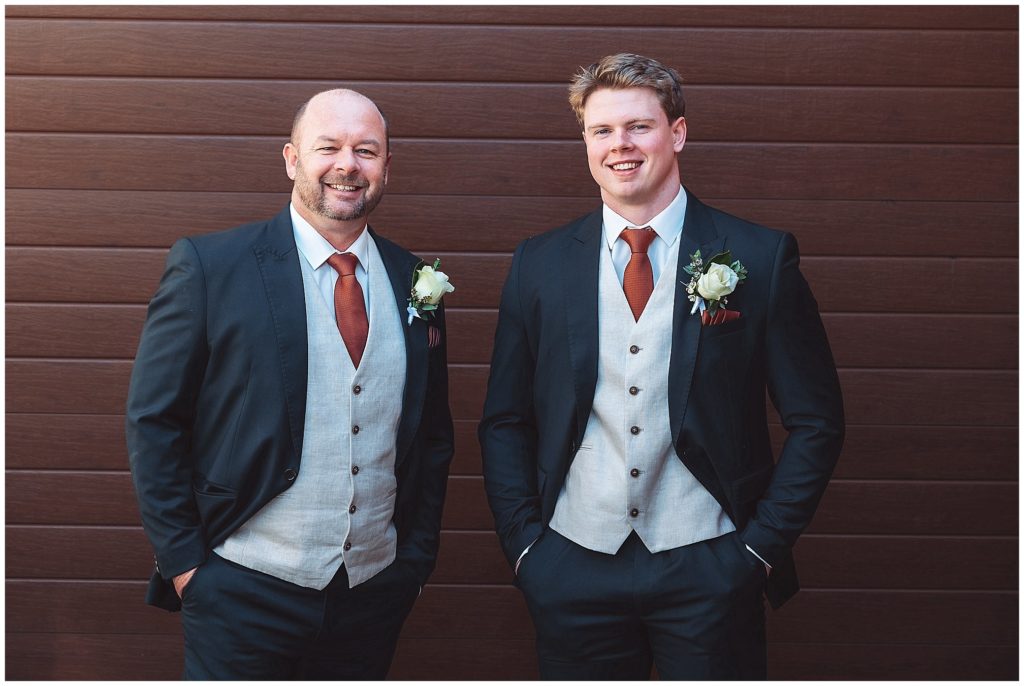 a groom and his son against a timber background hands in pockets in North Tamworth