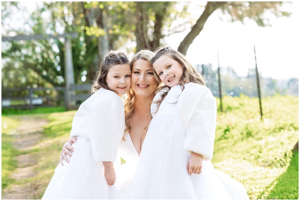 a bride and her girls cuddle in white fur coats with a green background