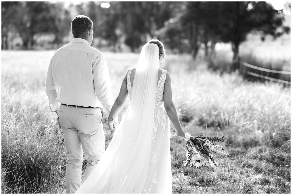 wedding photos a couple walk away in the long grass at Dathem park woolshed black and white photo