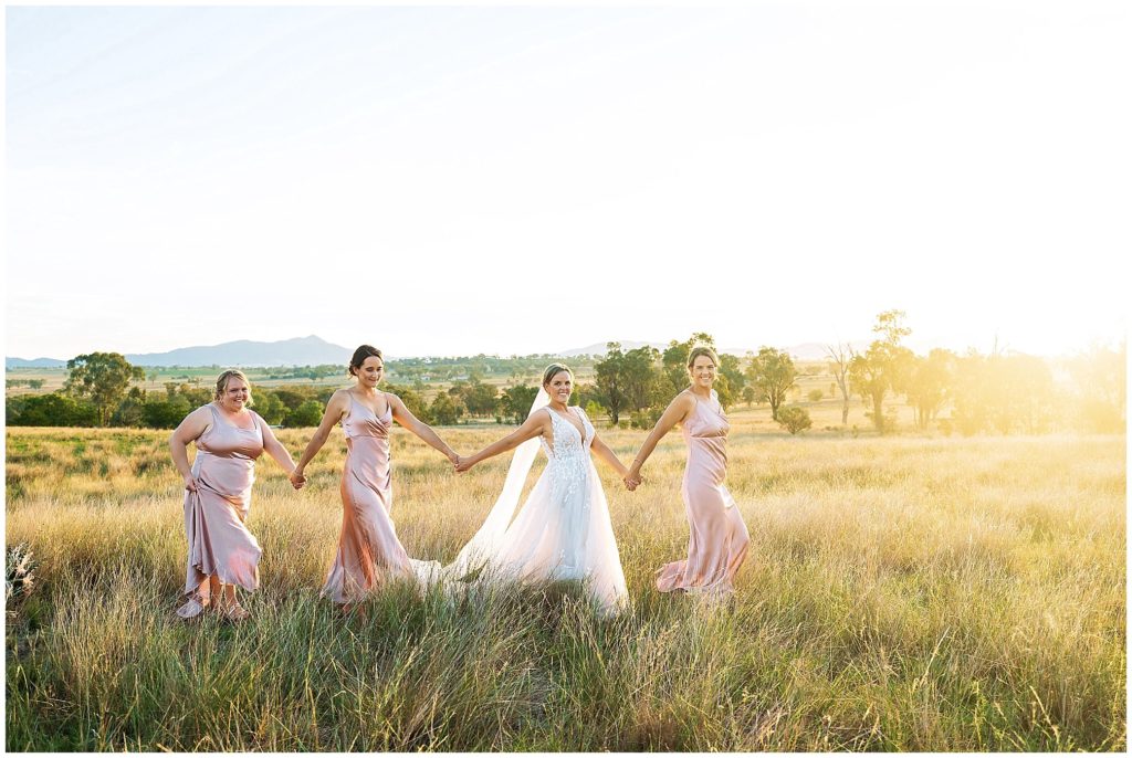 in the long grass at Dathem park woolshed as the sun sets and the bride & her bridesmaids walk hand in hand golden light Tamworth