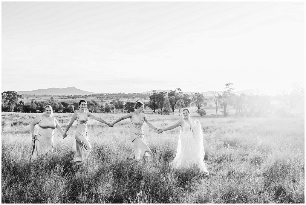 in the long grass at Dathem park woolshed as the sun sets and the bride & her bridesmaids walk hand in hand golden light Tamworth
