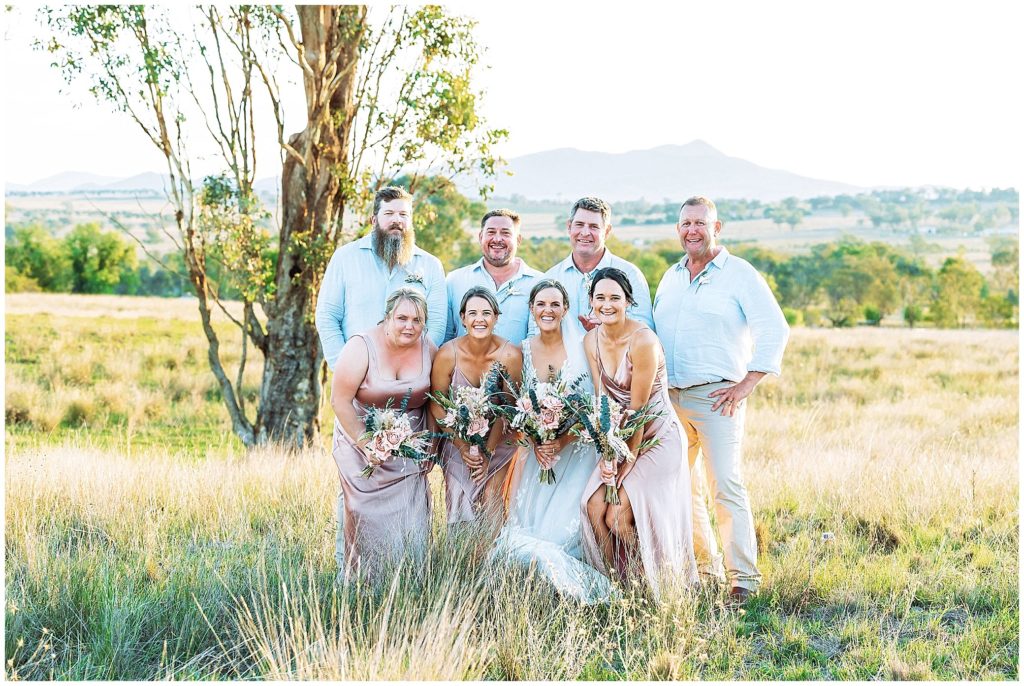 in the long grass on top of the hill at Dathem park wedding reception venue as a bridal party get photos as the sun sets