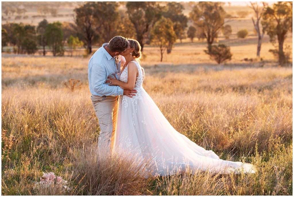 in the long grass on top of the hill at Dathem park wedding reception venue as as bride and groom kiss
