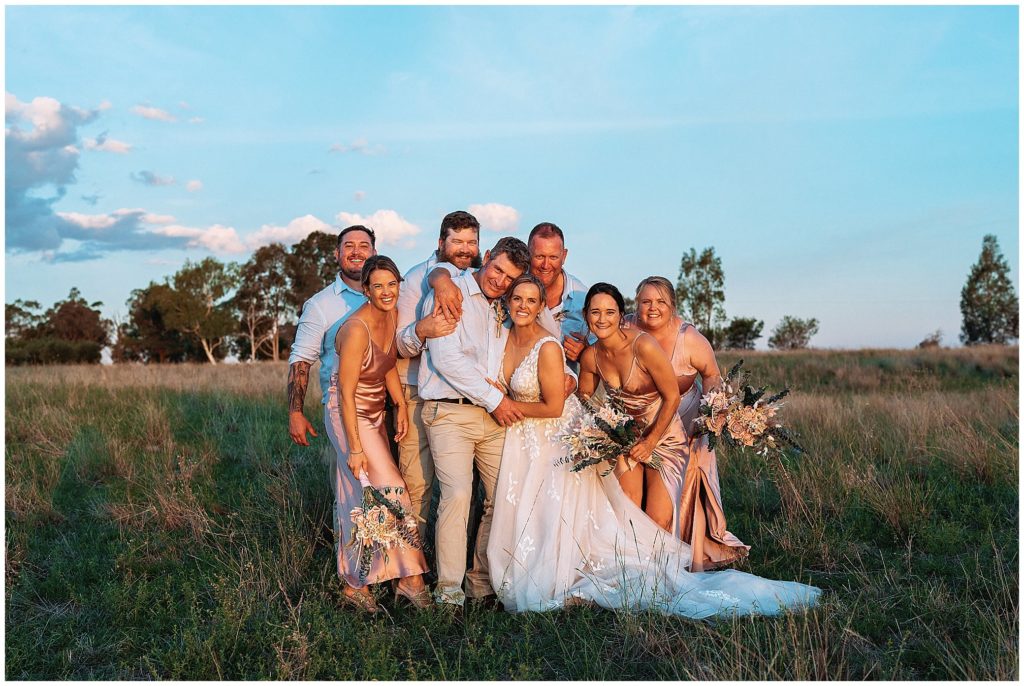 in the long grass on top of the hill at Dathem park wedding reception venue a bride & groom & the bridal party love & laugh as the golden sun sets over tamworth