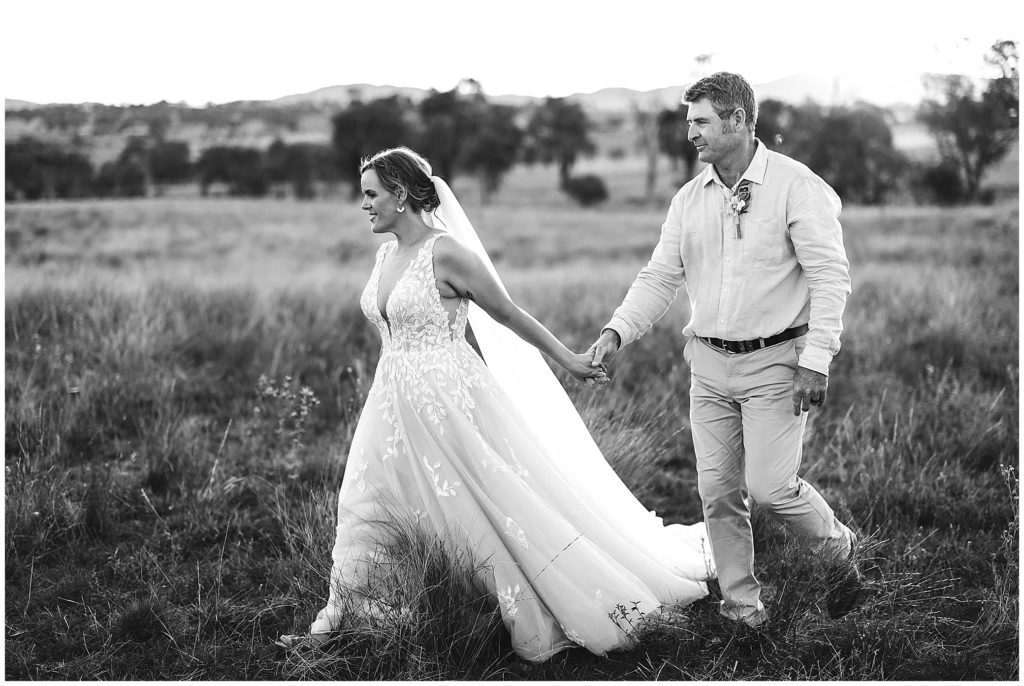 walking a bride & groom walk as the sun sets in long grass black & white