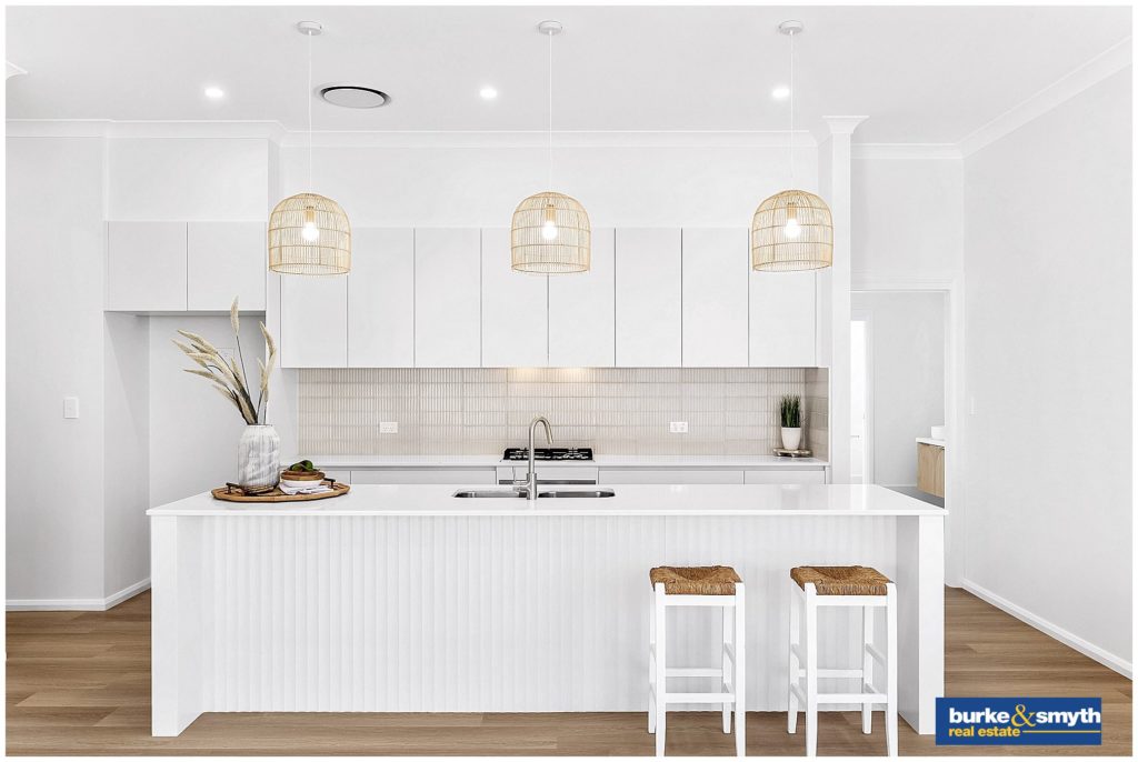 stunning white kitchen with cream tiles & rattan light shades that is part of a home for sale by Burke & smyth the real estate photographer, Karissa Tuckwell captures the light & timber in a white room. there is two stools to sit on under the bench