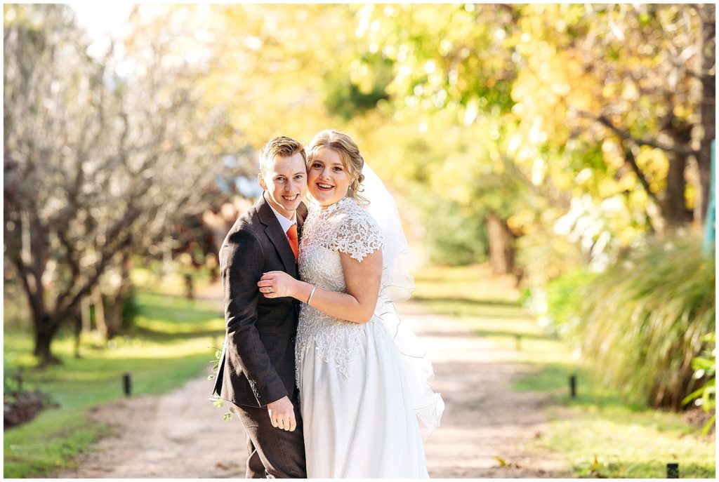 a bride and groom hug and smile on a roadway at Rock Abbey Gardens
