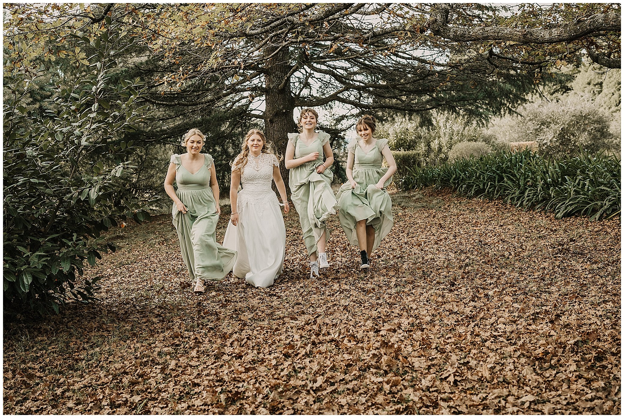 girls in mint green dresses skip under a big tree at a wedding