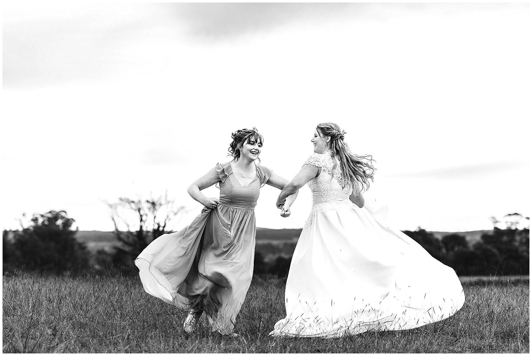 a bride and her sister spin and skip as the sunsets behind them on a wedding day at Rock Abbey Gardens Armidale black and white
