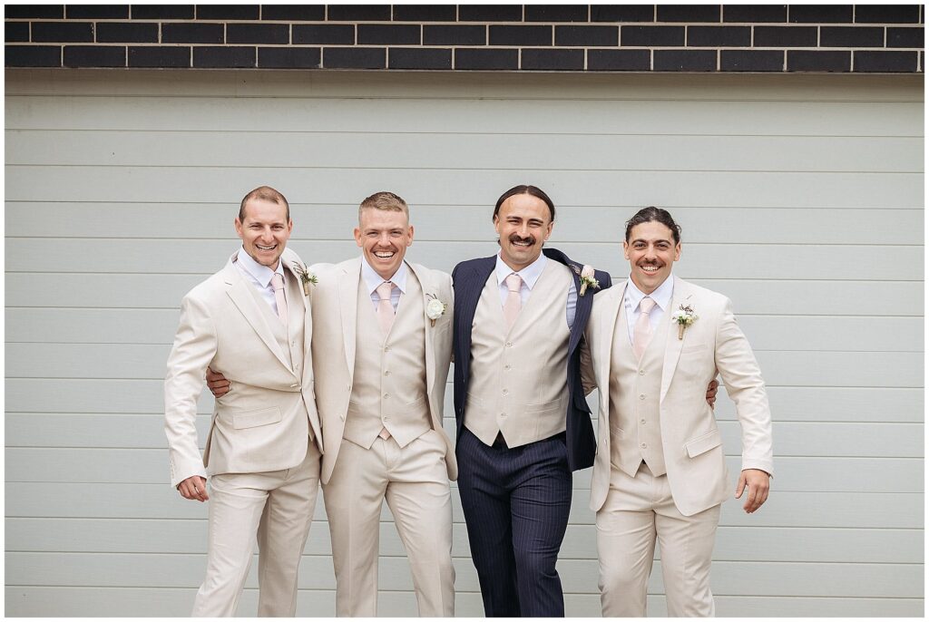 groomsman on a wedding day in cream suits smile an dlaugh at the camera before heading to church in Manills NSW