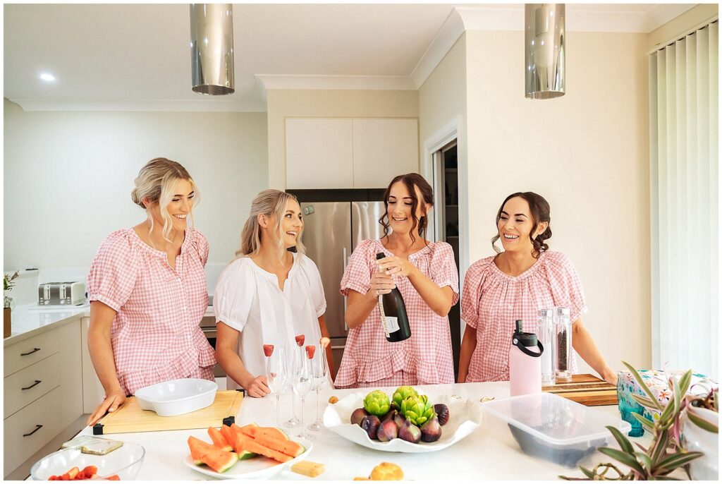 girls in pink pajamas whilst the bride wears white pops a bottle of bubbly on her wedding day