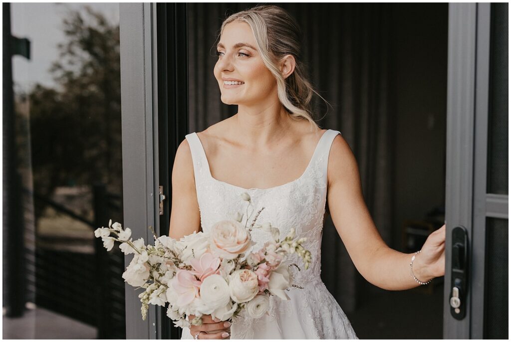 a bride holding her bouquet looks out the window as the breeze blows her hair
