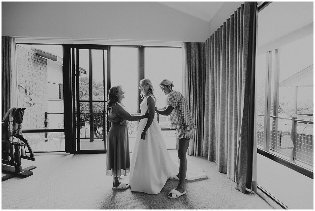a black and white photo of a bride gettiign ready with her mother and friend as the sun comes over a house in east tamworth NSW