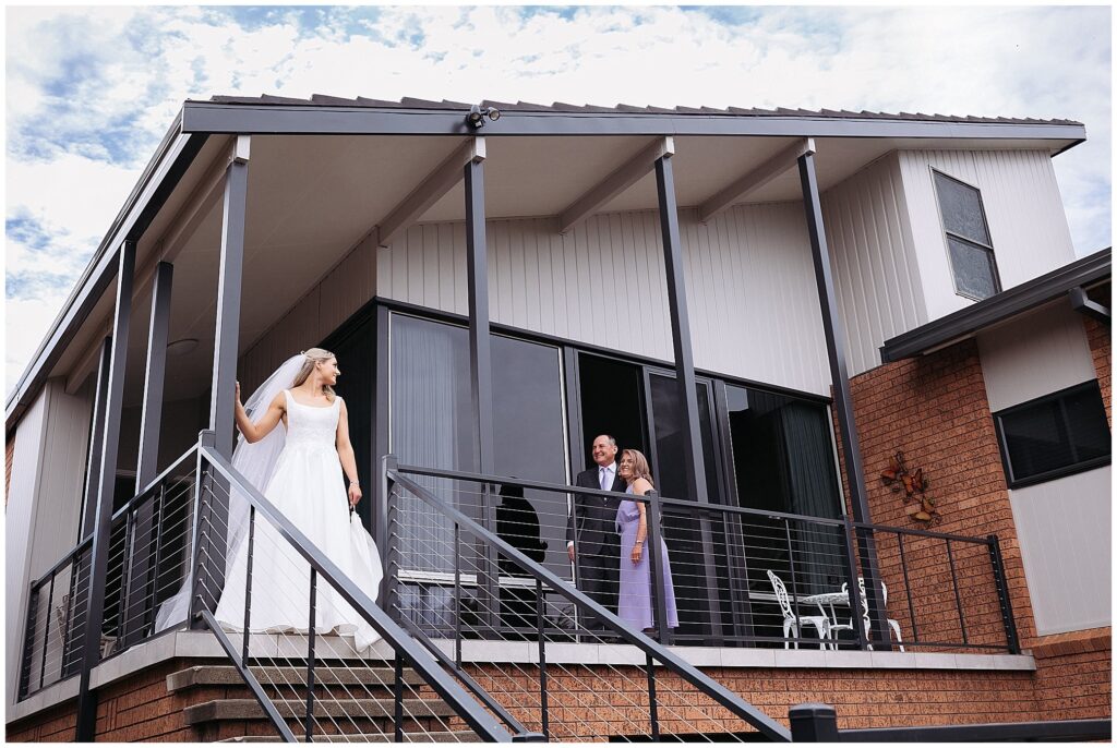 a mum and ad in East Tamworth Look on their daughter on her wedding day as they smile at each at the front of their house