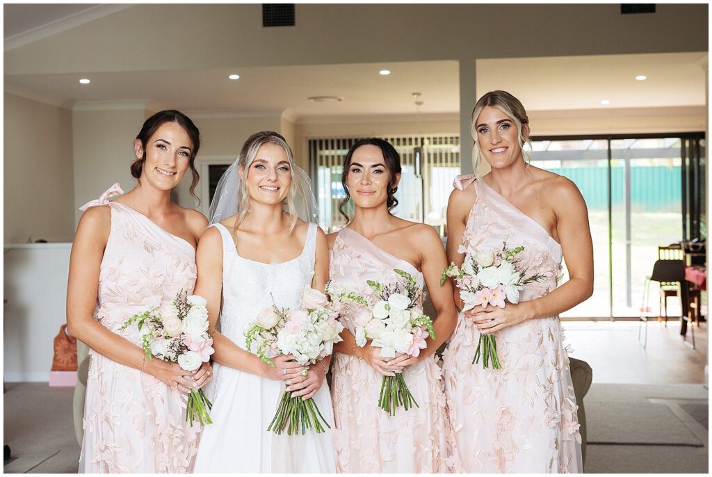 a bride and her bridesmaids in a pink dress smiel in a home