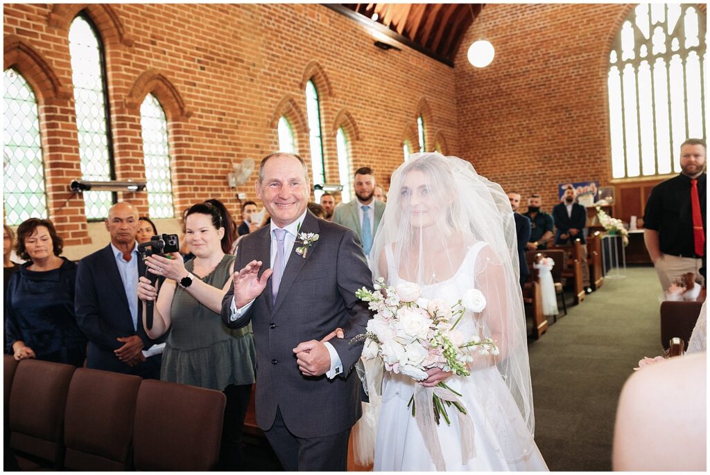a dad waves at the audience as he leads his daughter down the aisle