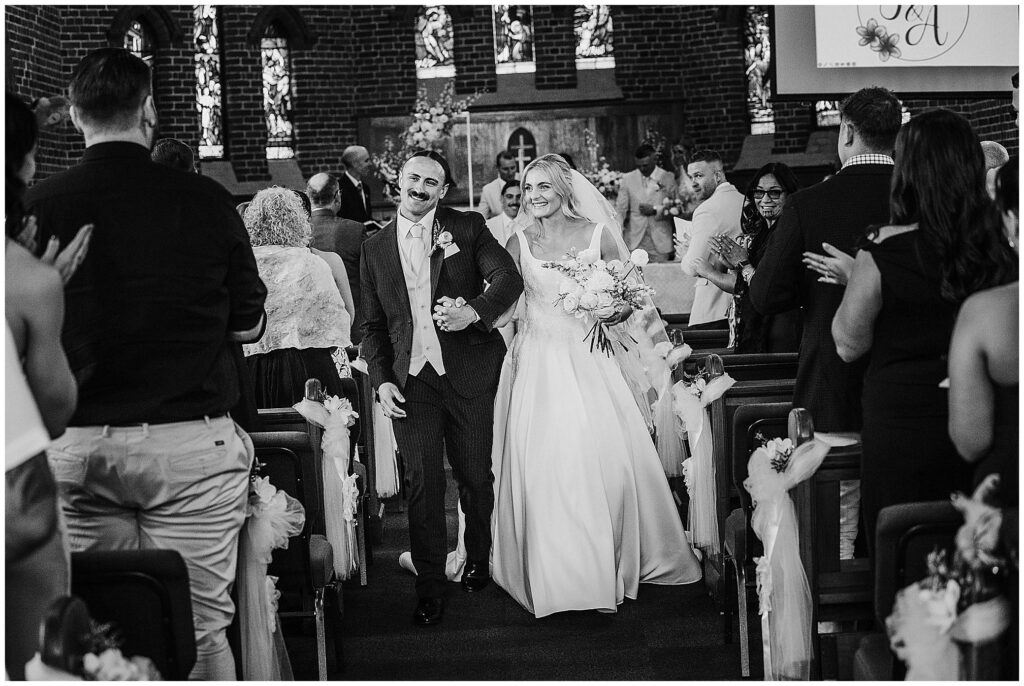 a couple leave the church in Manilla NSW as they smile at the guests black and white photo