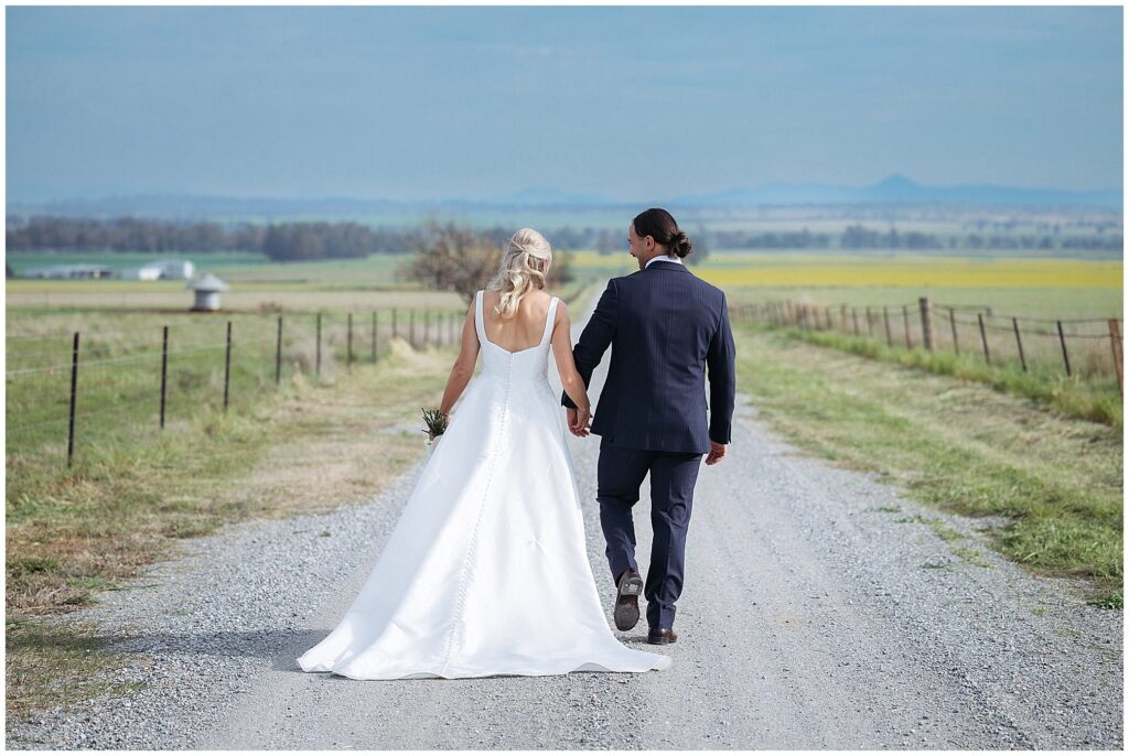 walking on a country road near Attunga nsw a couple in a wedding dress and suit holds hands there is a canola crop in the background